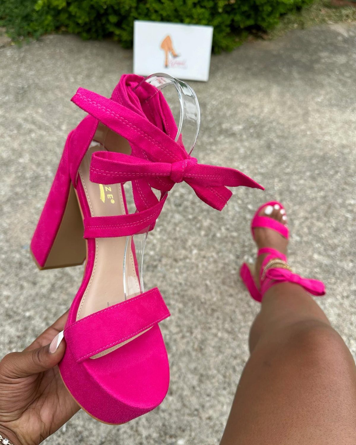 A person holding a bright pink platform sandal with a large bow and thick block heel.