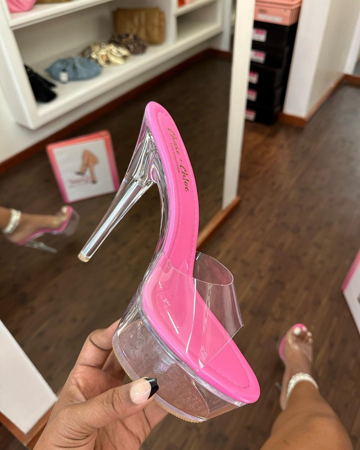 A hand holding a pink high heel sandal with a clear platform and clear stiletto heel.