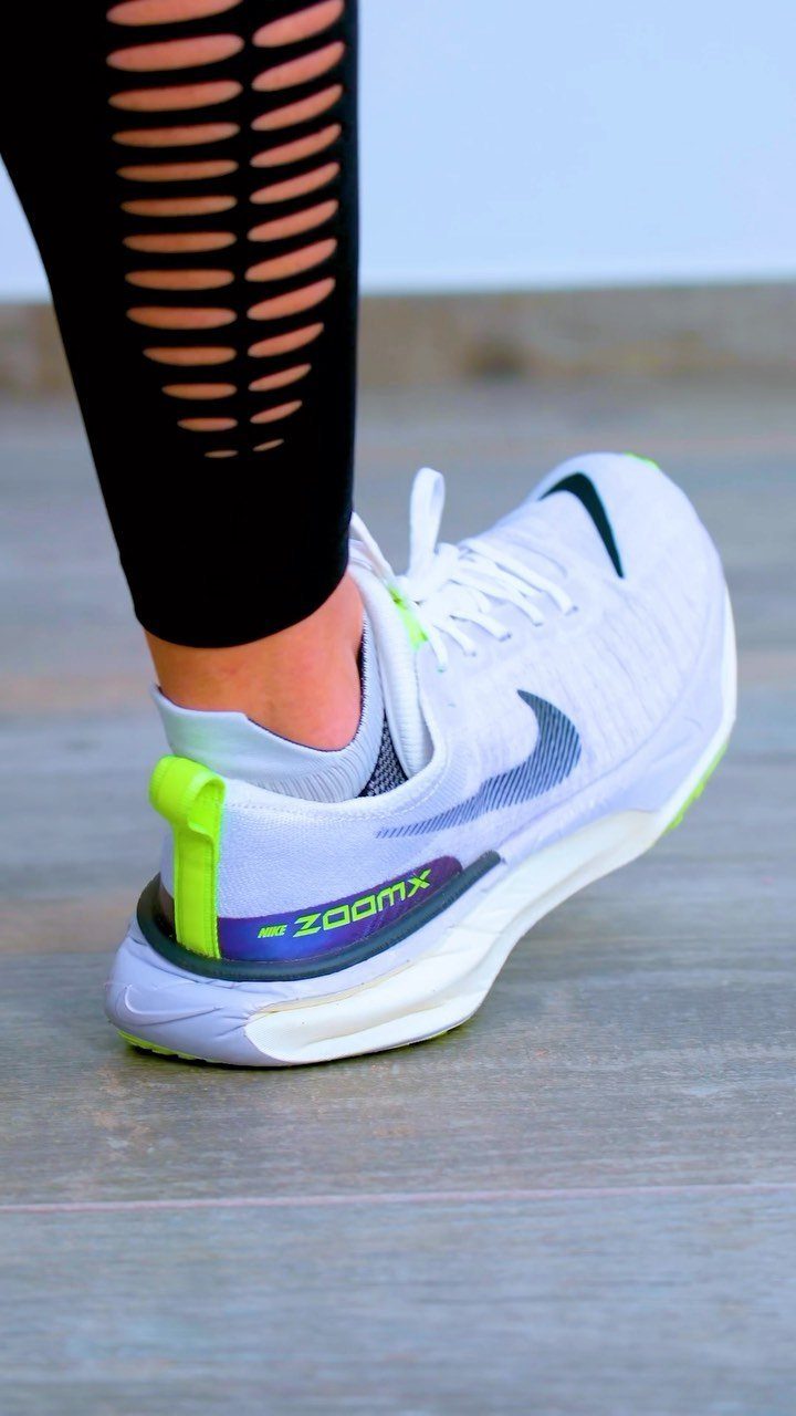 White Nike running shoe with blue and lime green accents on a wooden floor.