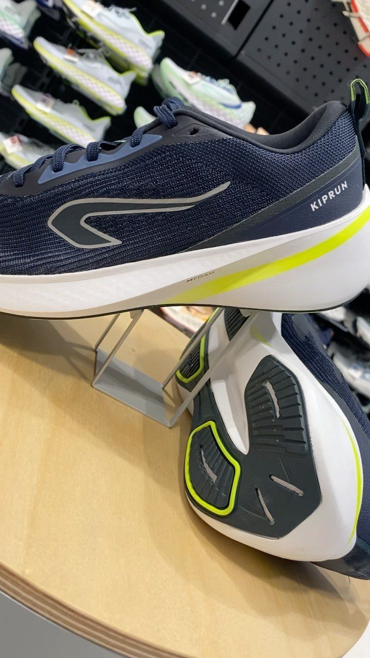 Navy blue Kiprun running shoes with lime green accents resting on a wooden retail display shelf.