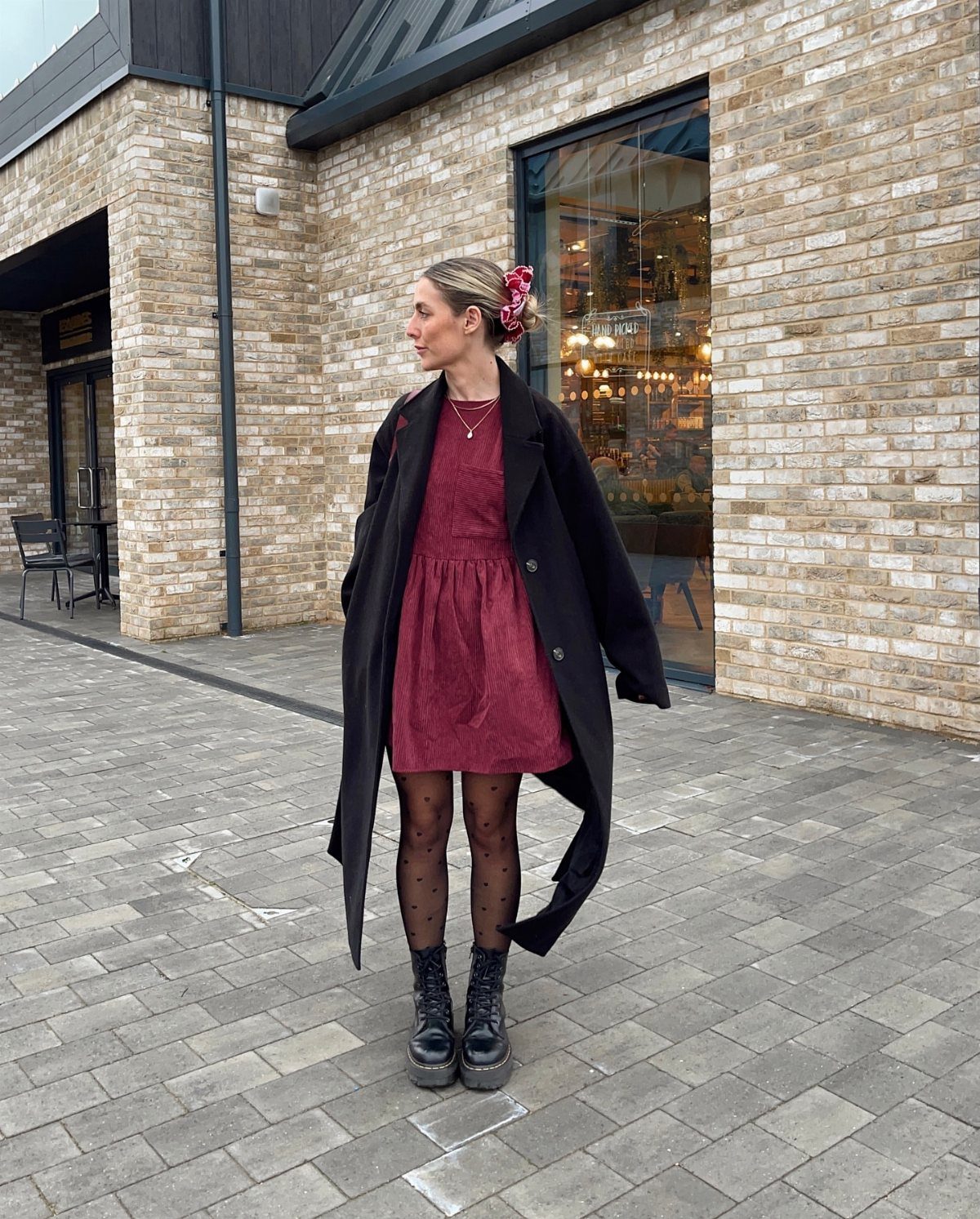 Woman wearing a red dress, black coat, patterned tights, and black chunky ankle boots.