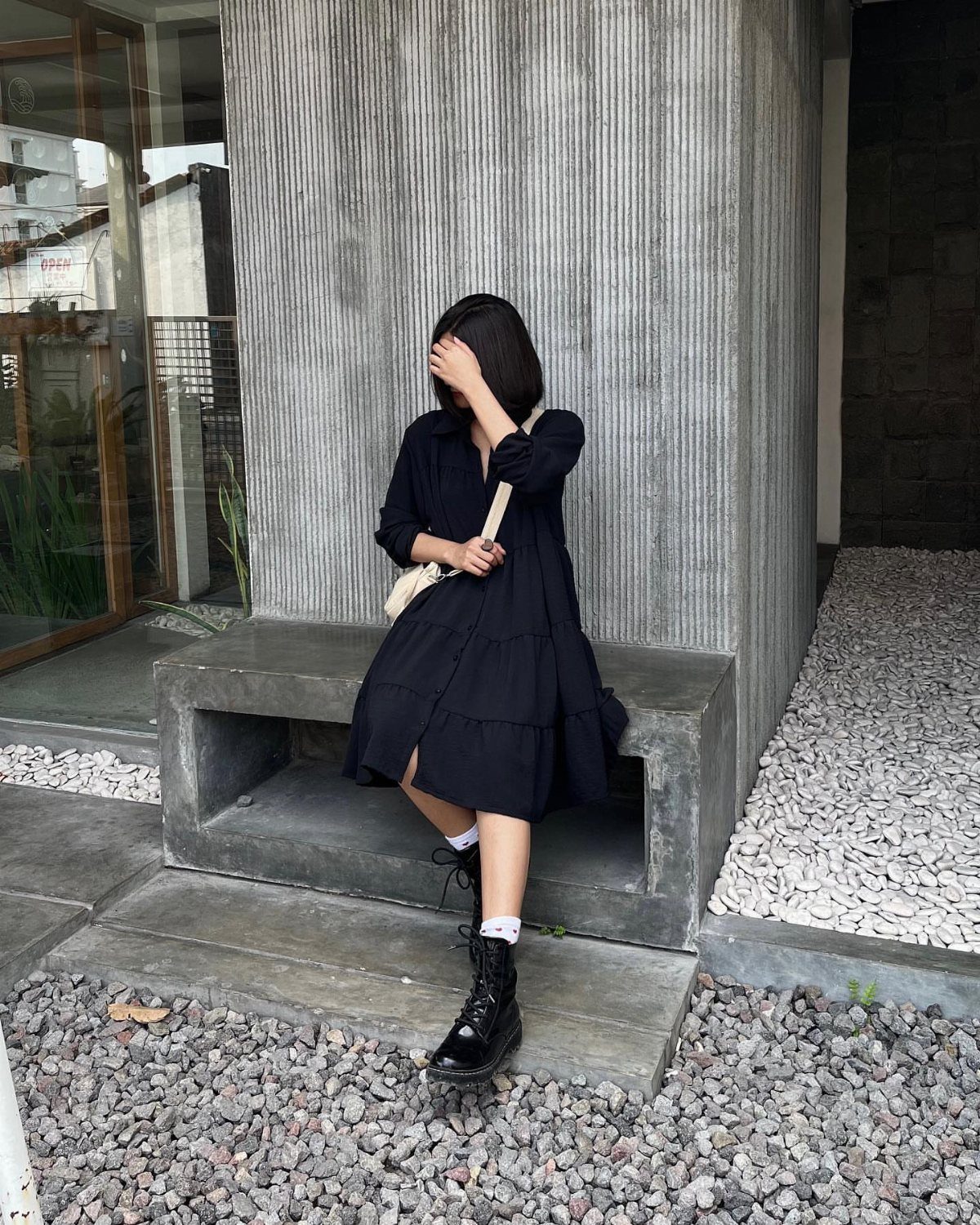 Person in a black tiered dress and black combat boots sitting on a concrete bench.
