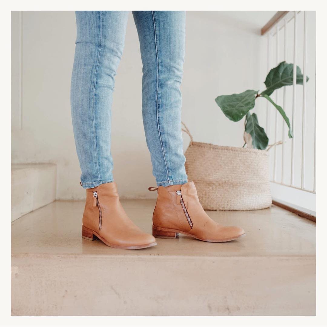Person wearing light blue skinny jeans and tan leather ankle boots standing on concrete steps.