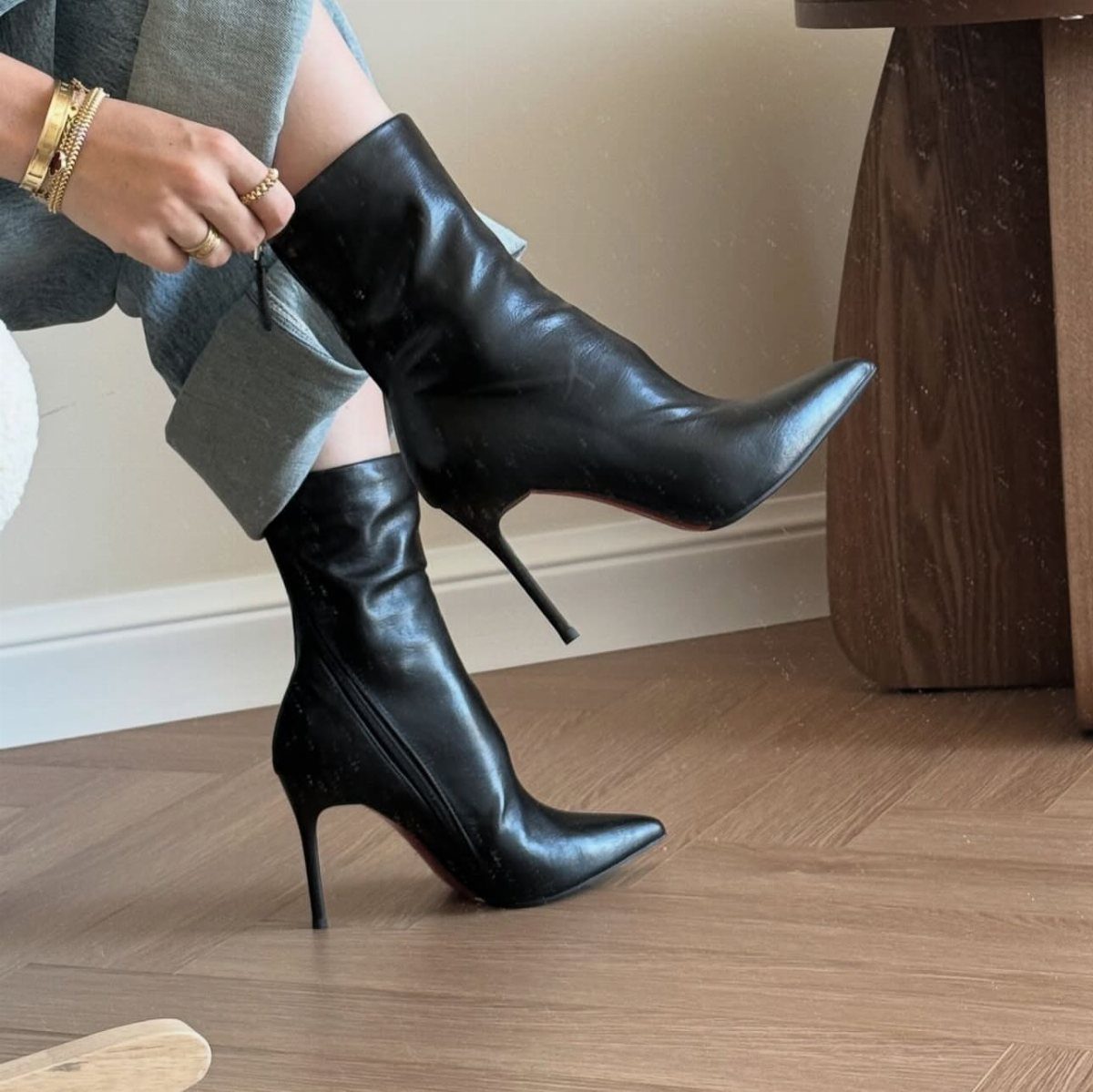 Black pointed-toe stiletto ankle boots worn with grey denim jeans on a wooden floor.
