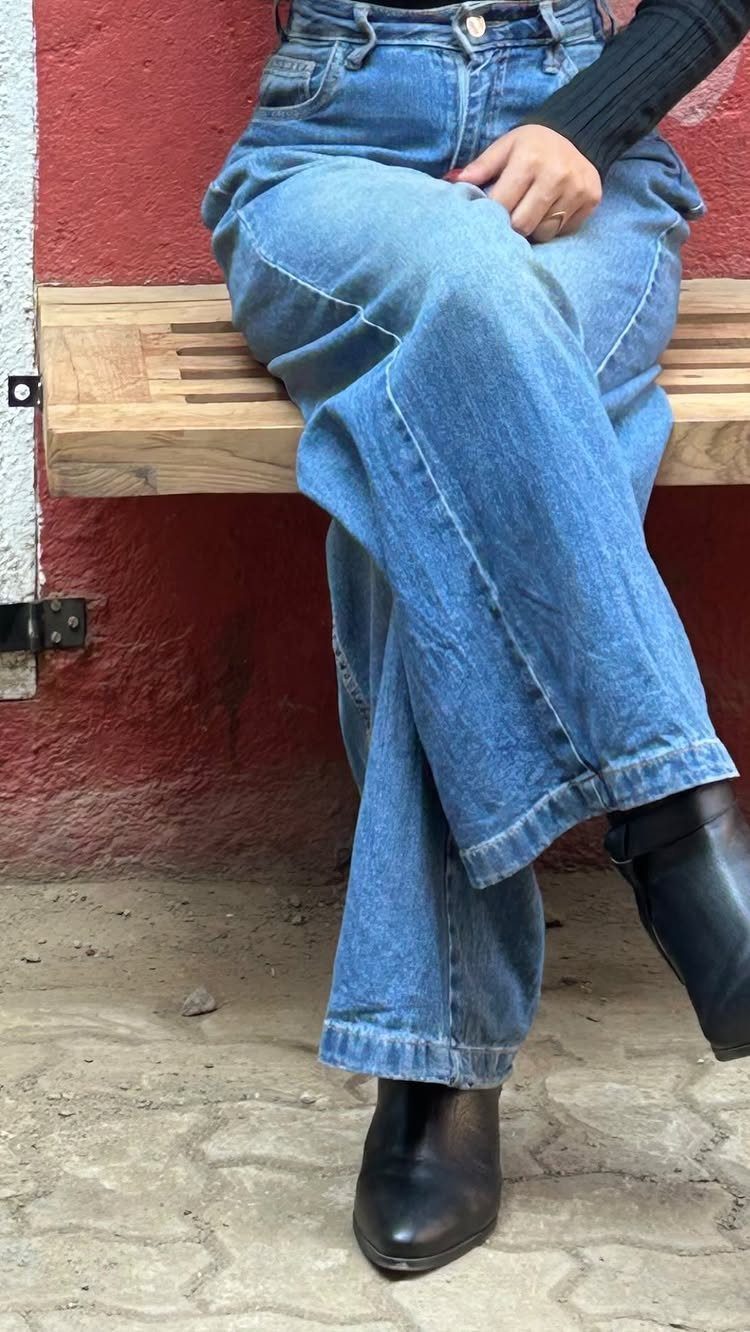 Person wearing wide-leg blue jeans and black leather ankle boots sitting on a wooden bench.