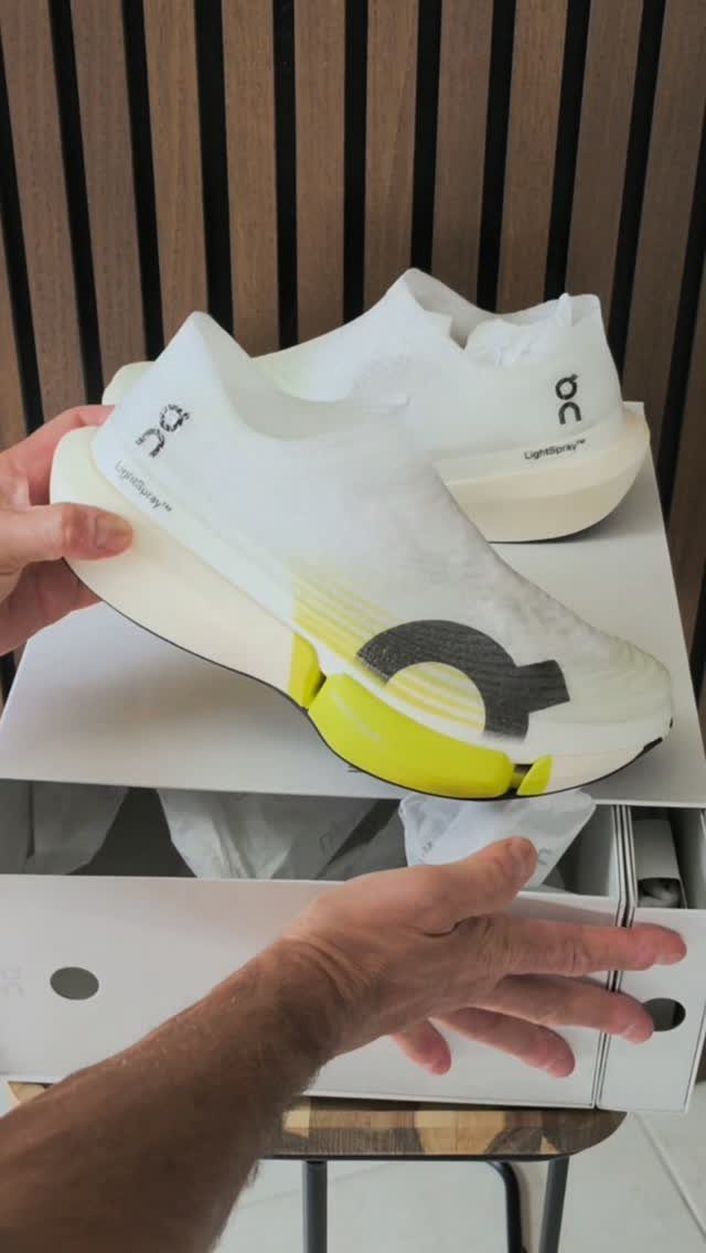 A person holding a white and yellow On running shoe with a thick cushioned sole.
