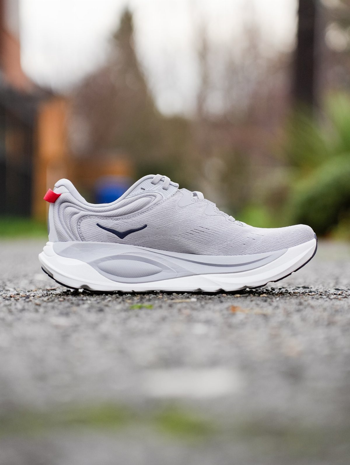 Light grey Hoka athletic shoe with a thick white sole resting on gravel outdoors.