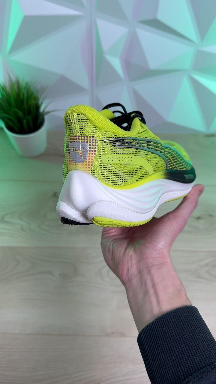 A hand holding a lime green mesh running shoe with a thick white sole.