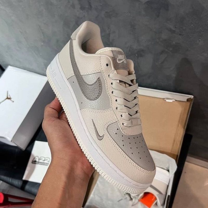 A hand holding a beige Nike Air Force 1 sneaker with a grey swoosh.