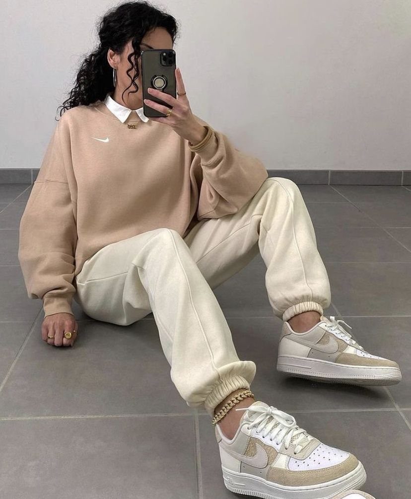 Person sitting on the floor wearing a beige sweatshirt, cream sweatpants, and beige sneakers.