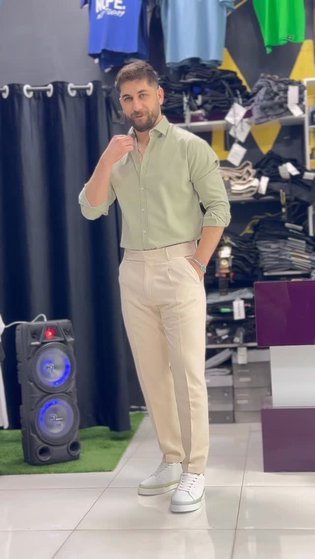Man wearing a light green shirt, beige trousers, and white leather sneakers standing in a shop.