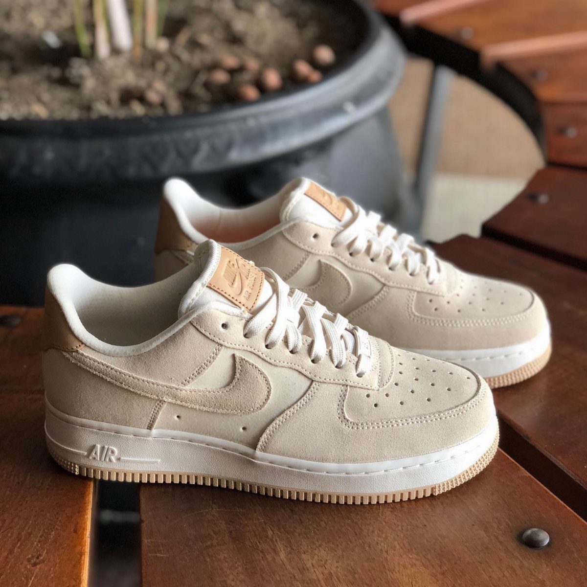 Beige Nike Air Force 1 sneakers with cream suede uppers sitting on a wooden bench.