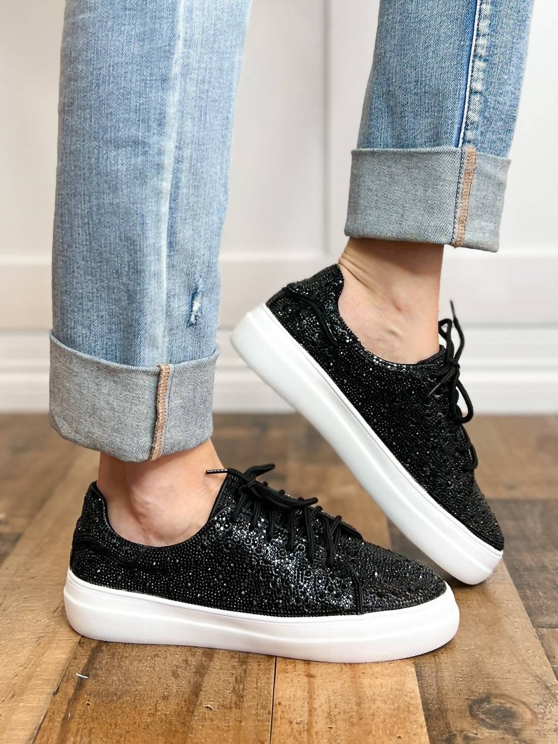 Black rhinestone platform sneakers with white soles worn with light blue cuffed denim jeans.