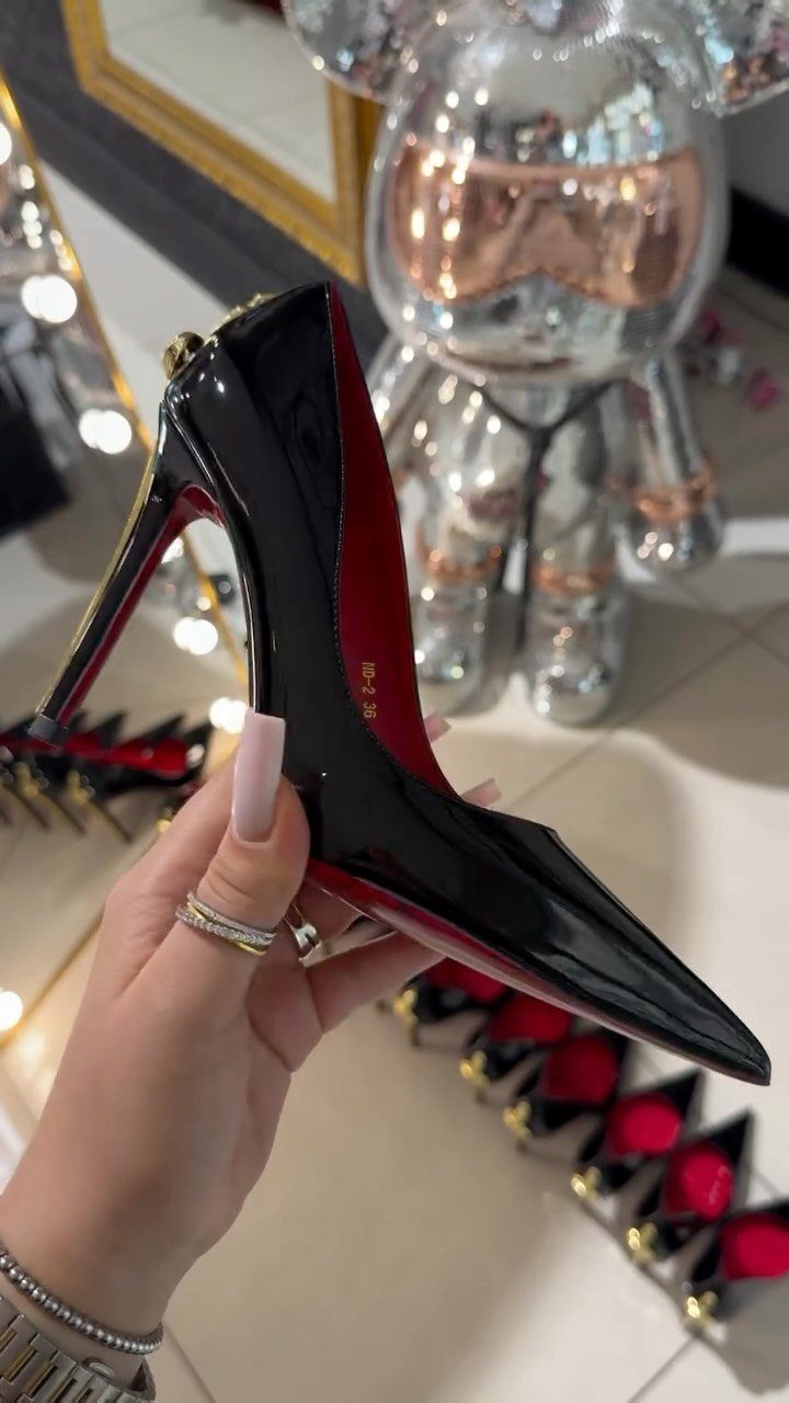 A hand holding a shiny black patent leather pointed-toe stiletto pump with a red sole.