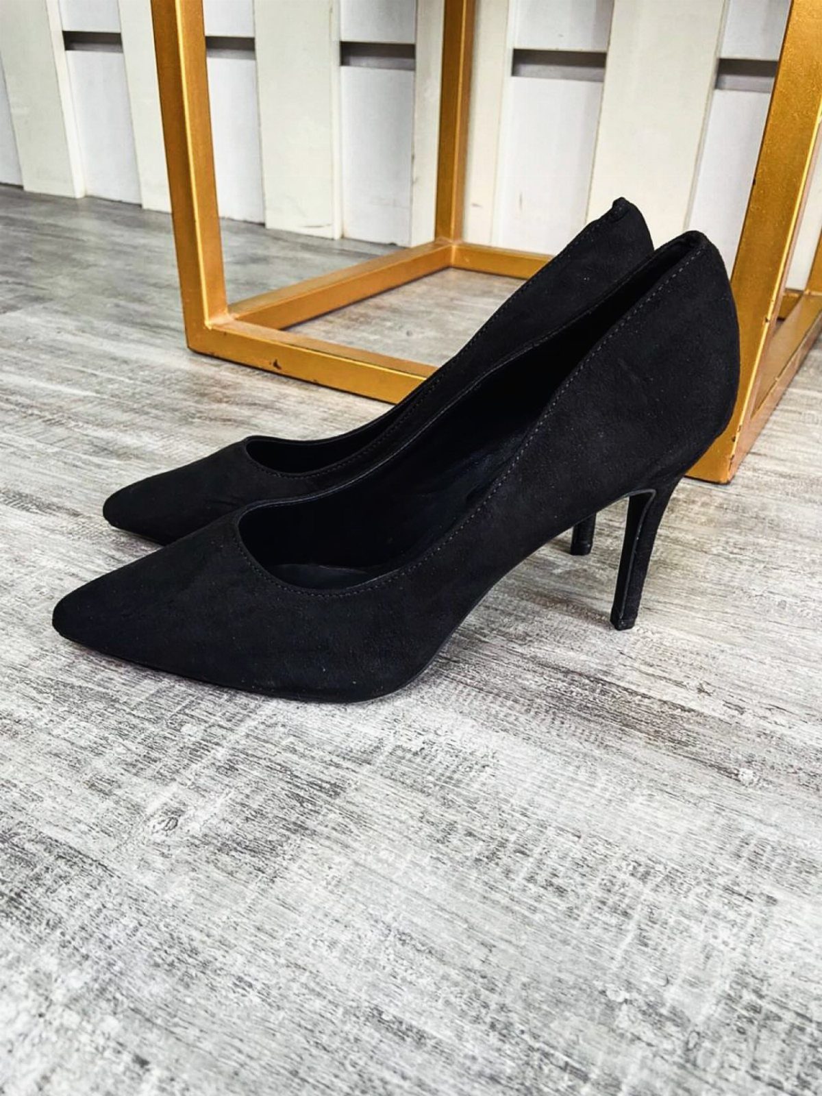 Black suede pointed-toe high heel pumps sitting on a grey wooden floor.