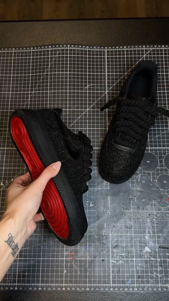 A hand holds a black glitter sneaker showing its bright red bottom sole.