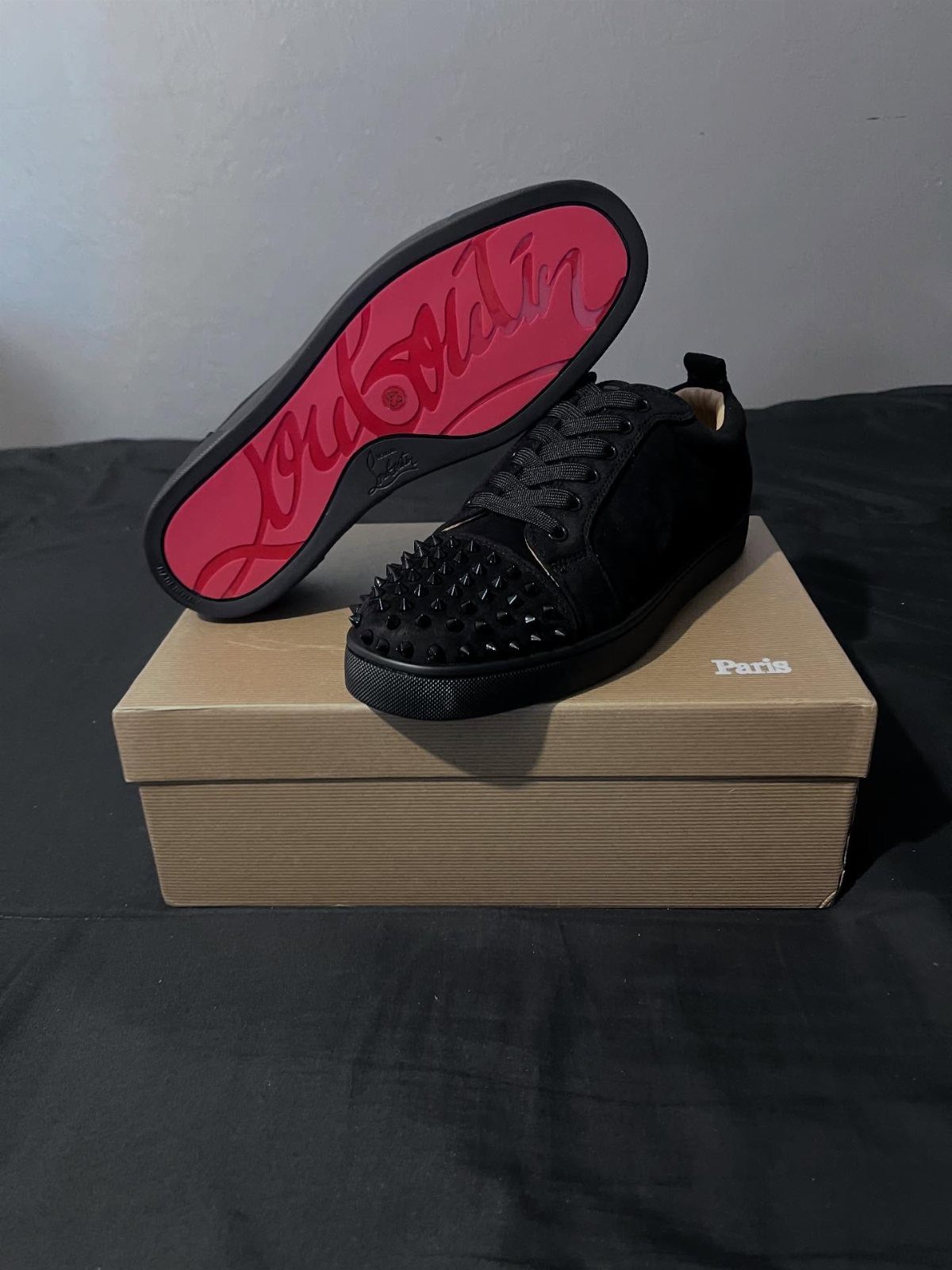 Black studded sneakers with bright red soles resting on a cardboard box.