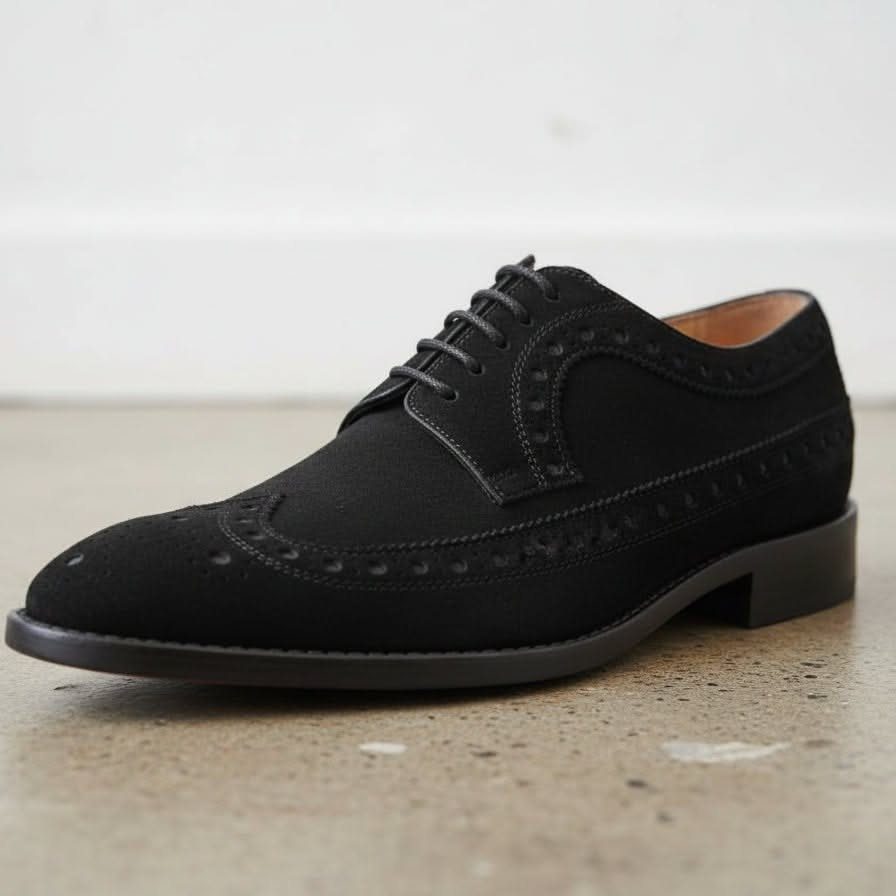 Black suede derby oxford shoe with brogue detailing on a light grey surface.