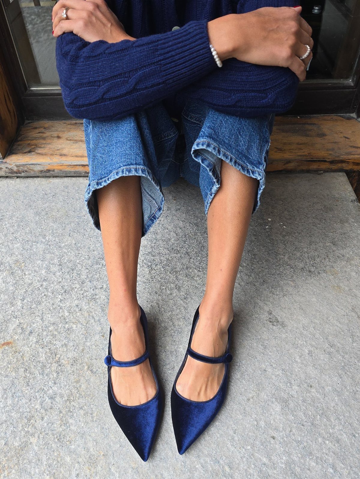 Person wearing navy blue velvet Mary Jane shoes and blue denim jeans sitting outdoors.