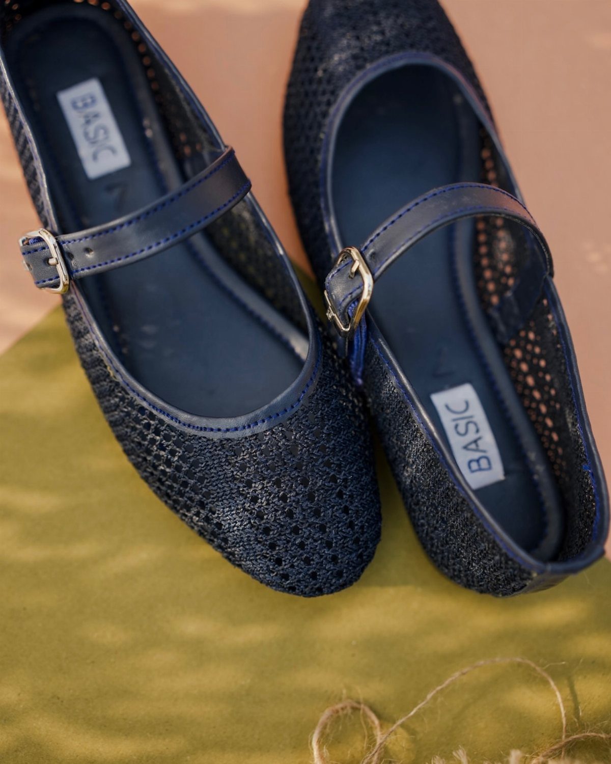 Navy blue textured Mary Jane flats with thin straps and gold buckles on green fabric.