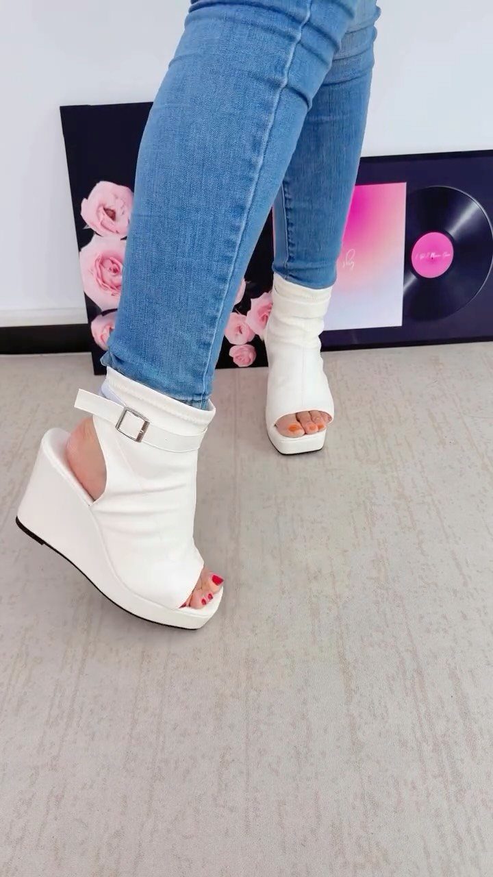 Person wearing white wedge peep-toe boots with an open back design and blue jeans.
