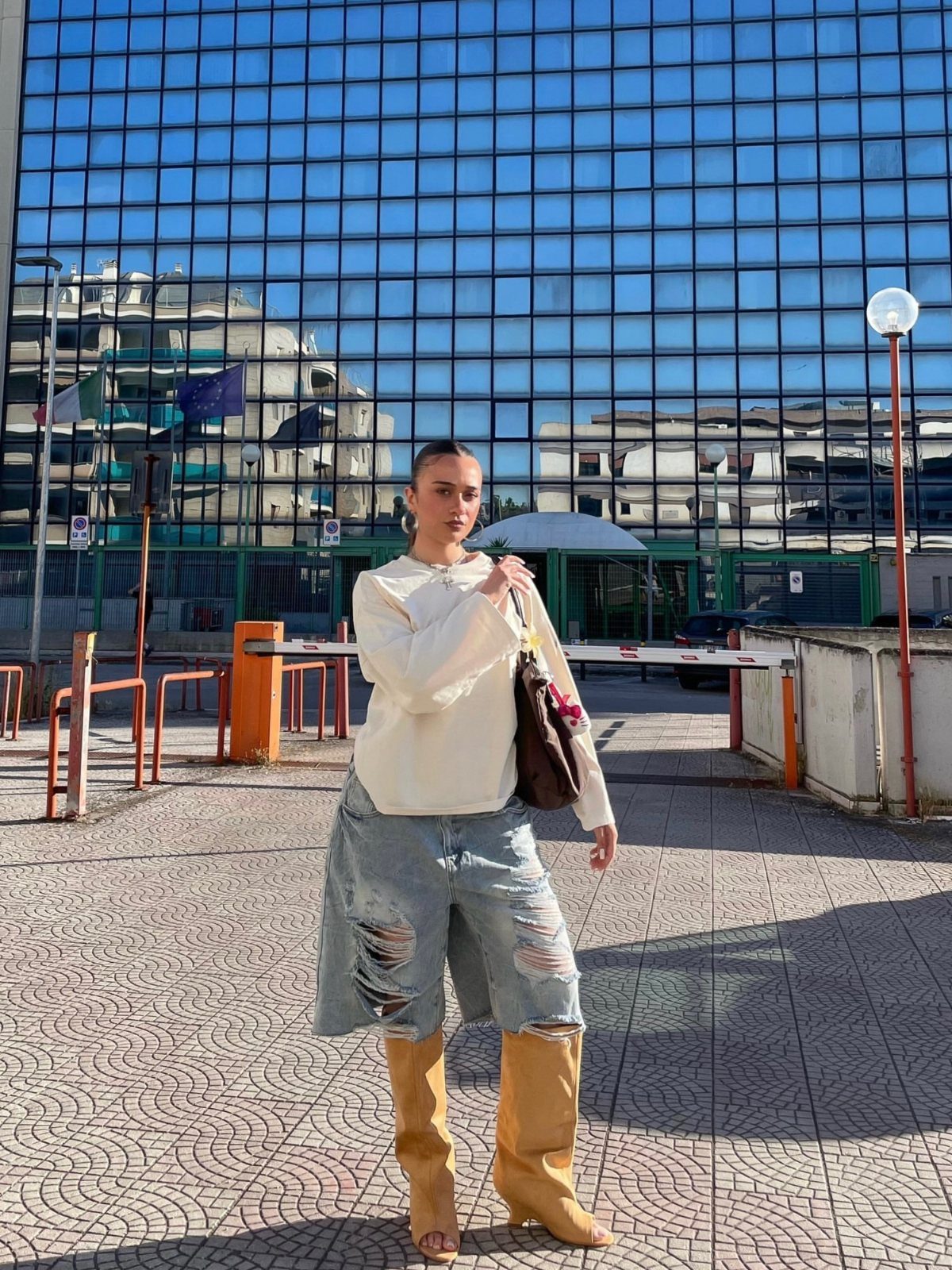 Woman wearing cream top, denim skirt, and tan thigh-high peep toe boots standing outdoors.