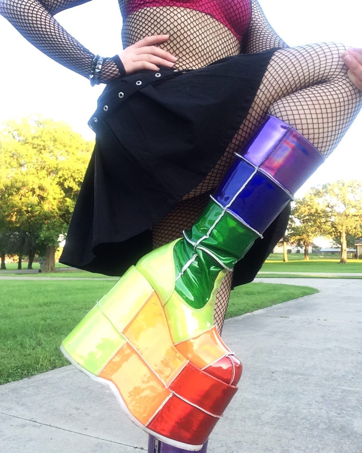 A person wearing colorful, glossy platform boots and fishnet stockings while posing outdoors.