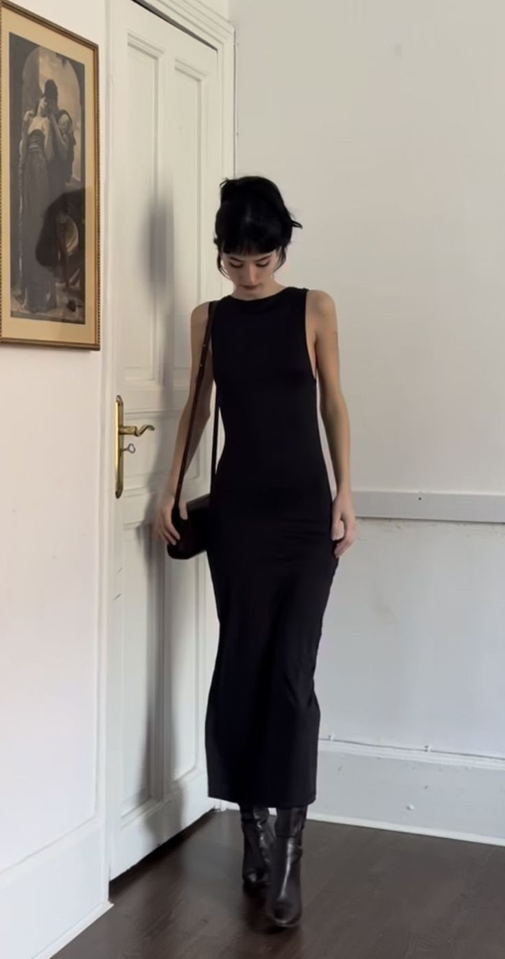 Woman wearing a long black sleeveless dress paired with dark leather ankle boots indoors.