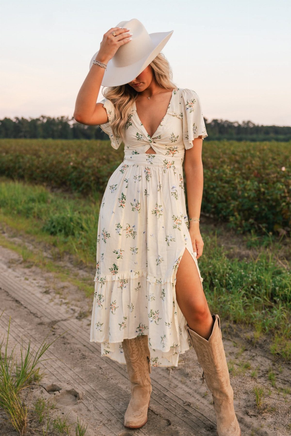 Woman in a white floral midi dress and tan cowboy boots standing in a field.