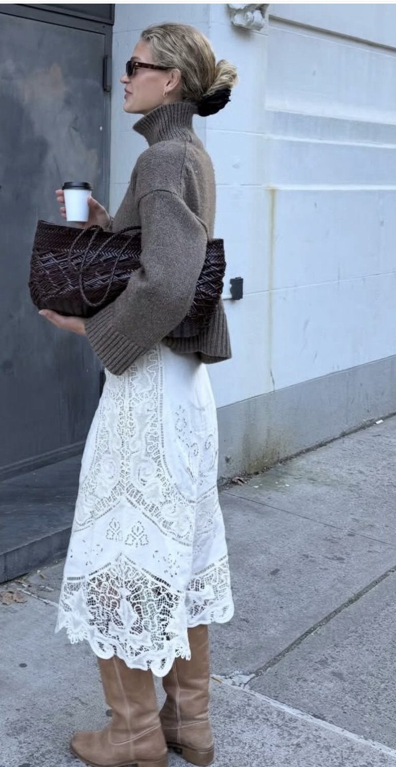 Woman wearing a white lace dress paired with tall tan suede boots on a city sidewalk.