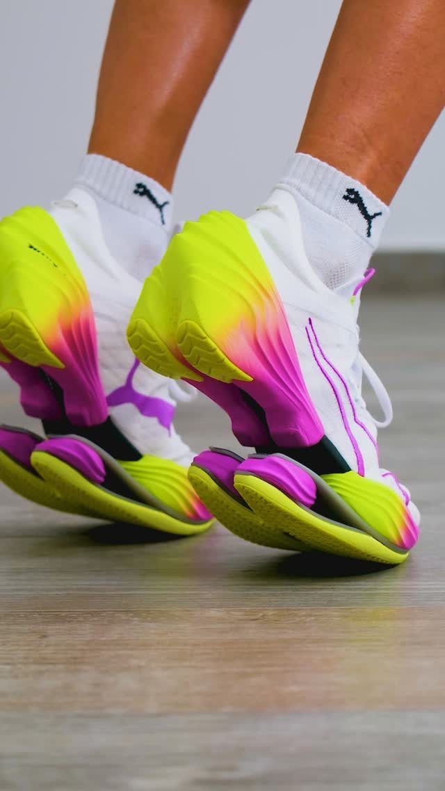 White and pink Puma running shoes with thick, segmented lime green midsoles on a wooden floor.