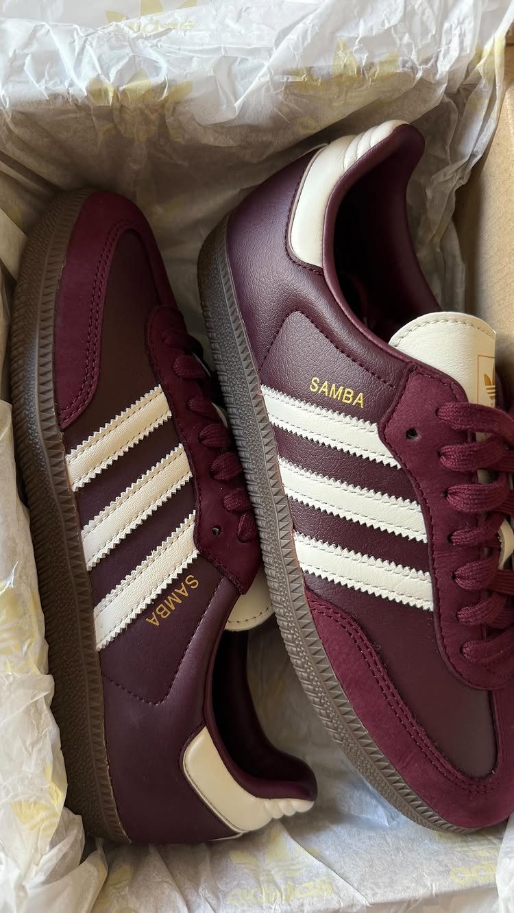 Burgundy Adidas Samba sneakers with white stripes sitting in a box with white tissue paper.