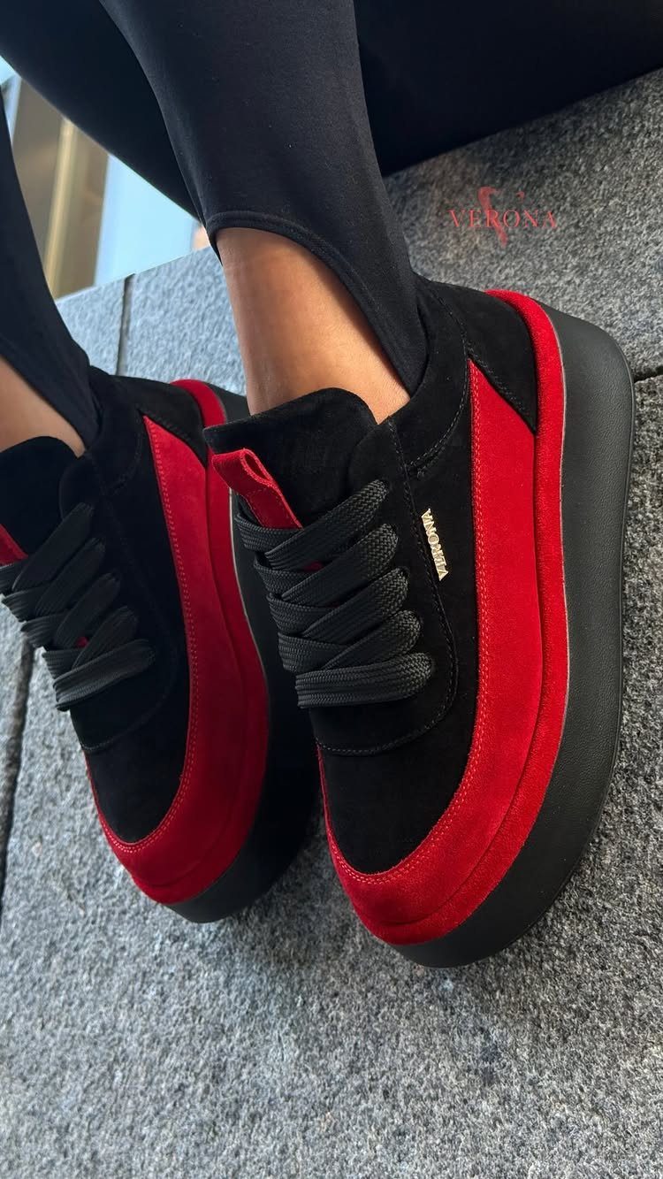 Black and red chunky platform sneakers worn by a person sitting on a stone ledge.