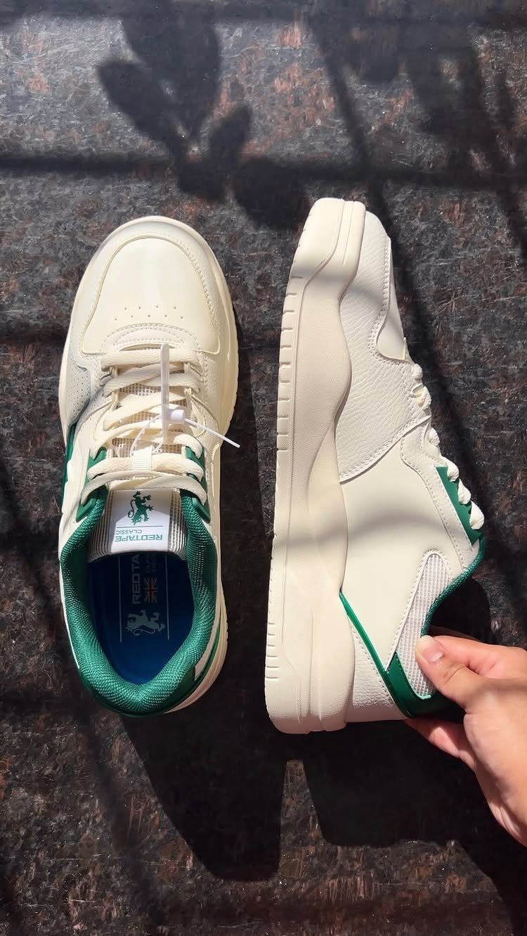 Cream and green retro-style sneakers resting on a dark, textured stone surface with shadows.