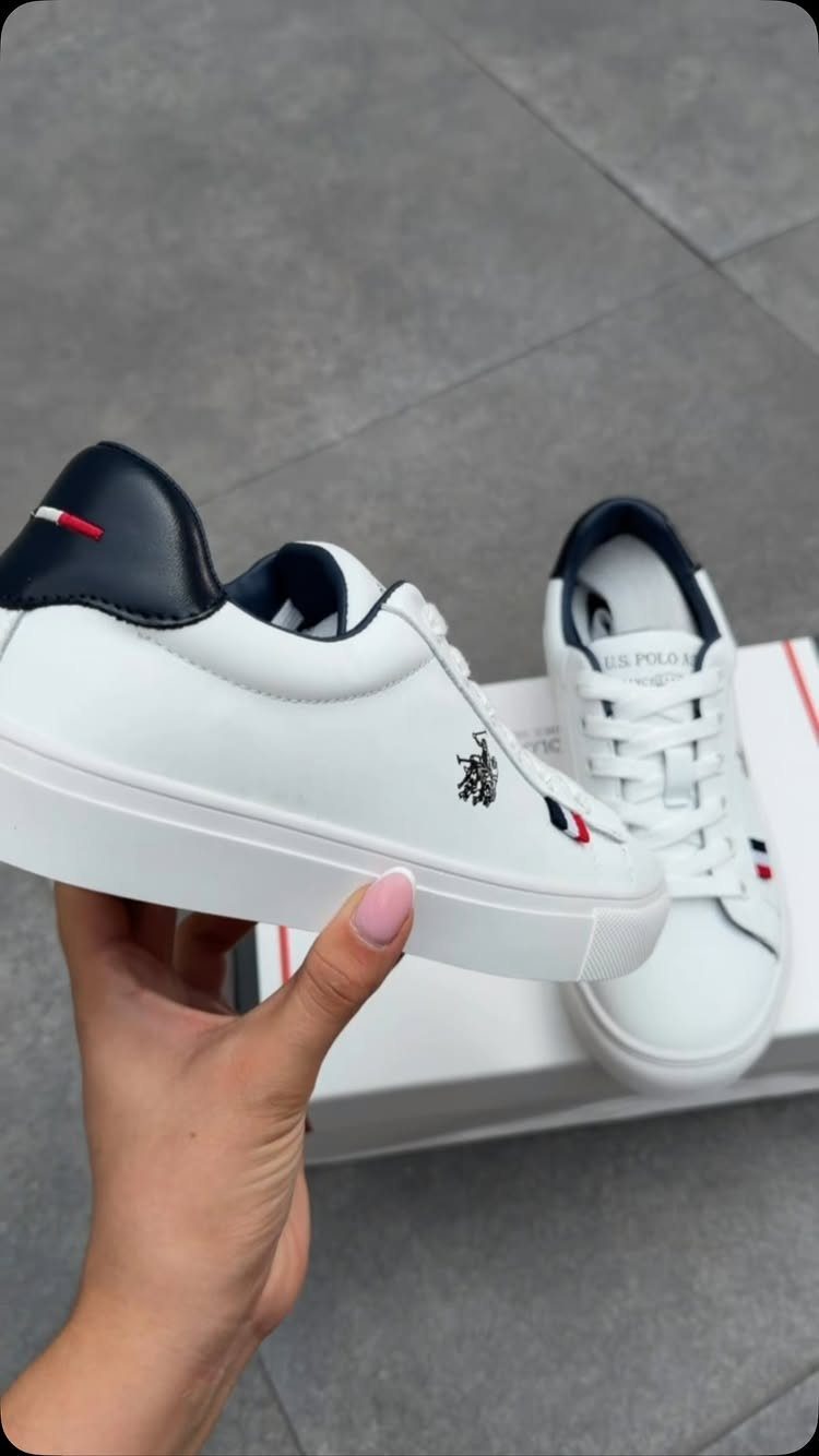 White low-top sneakers with navy blue accents held in a hand over a shoebox.