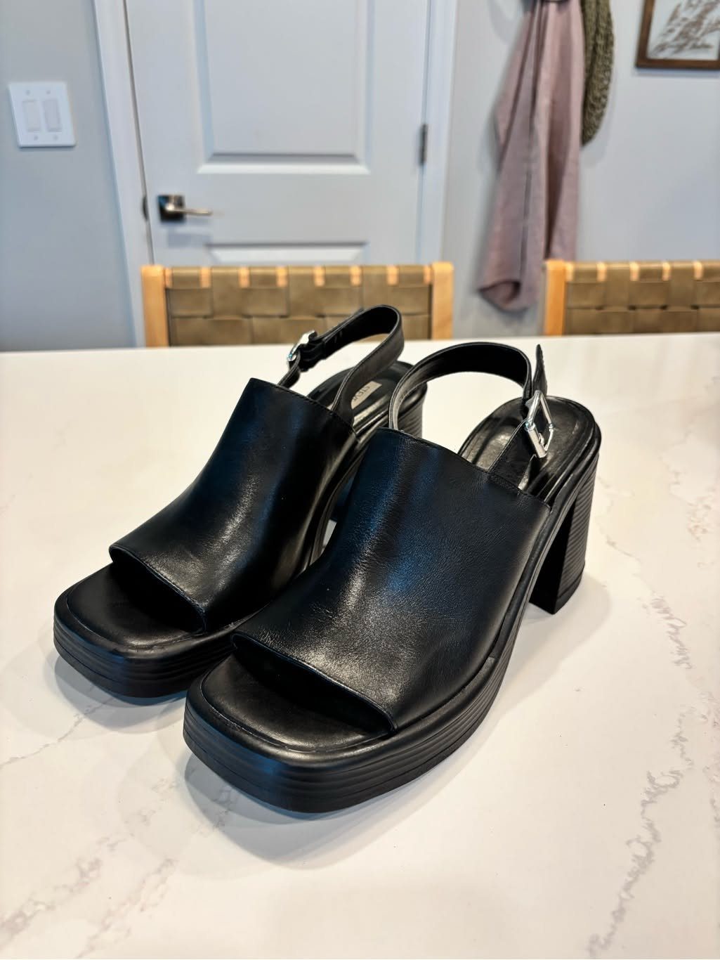 Black leather platform slingback sandals with chunky block heels on a white marble surface.