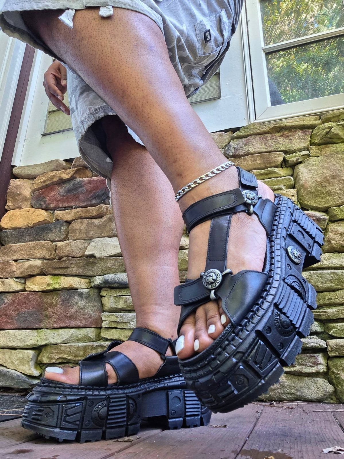 Person wearing chunky black platform sandals with silver metal ring buckles and thick textured soles.