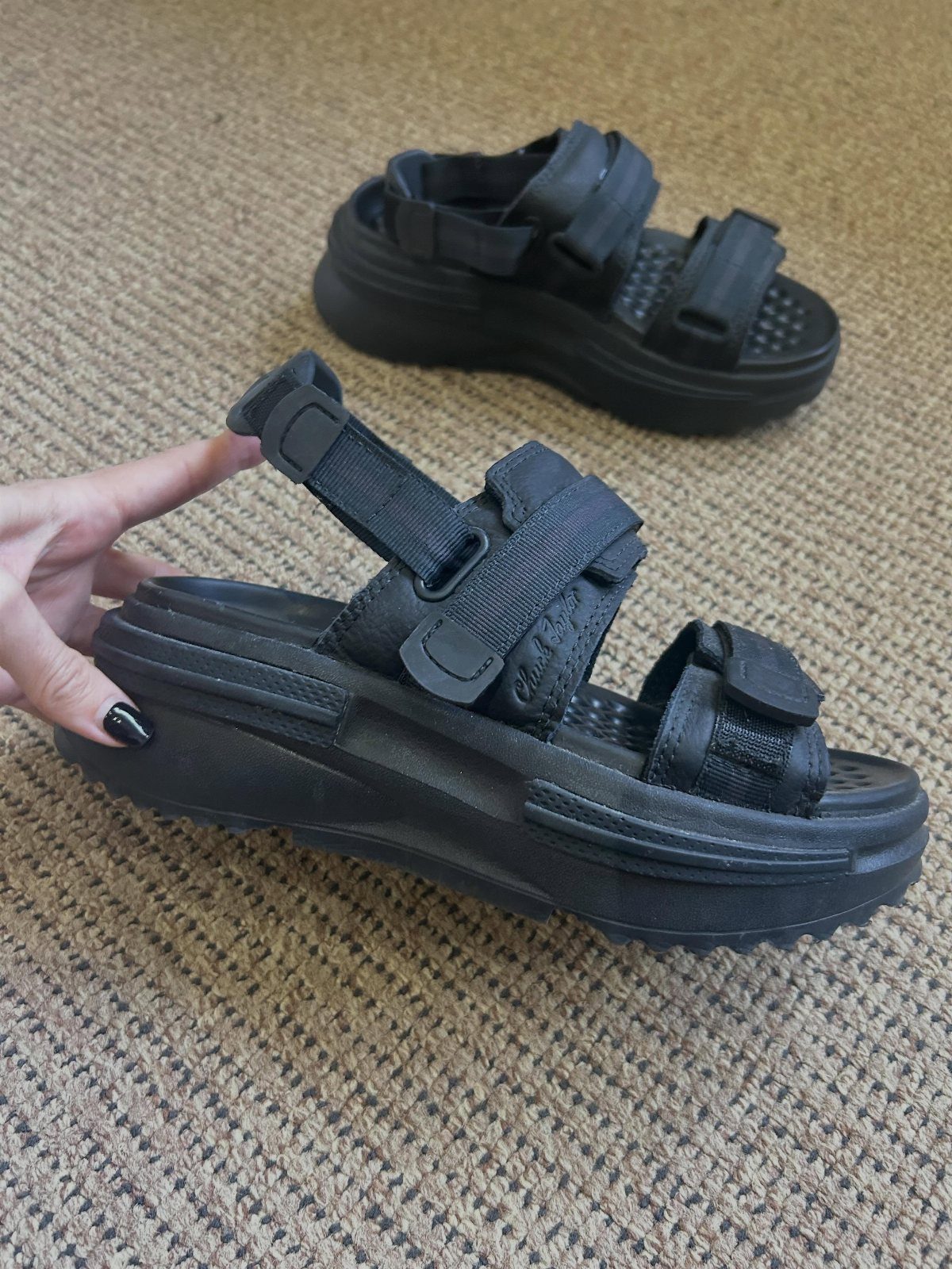 Black chunky platform sandals with wide velcro straps resting on a beige carpeted floor.