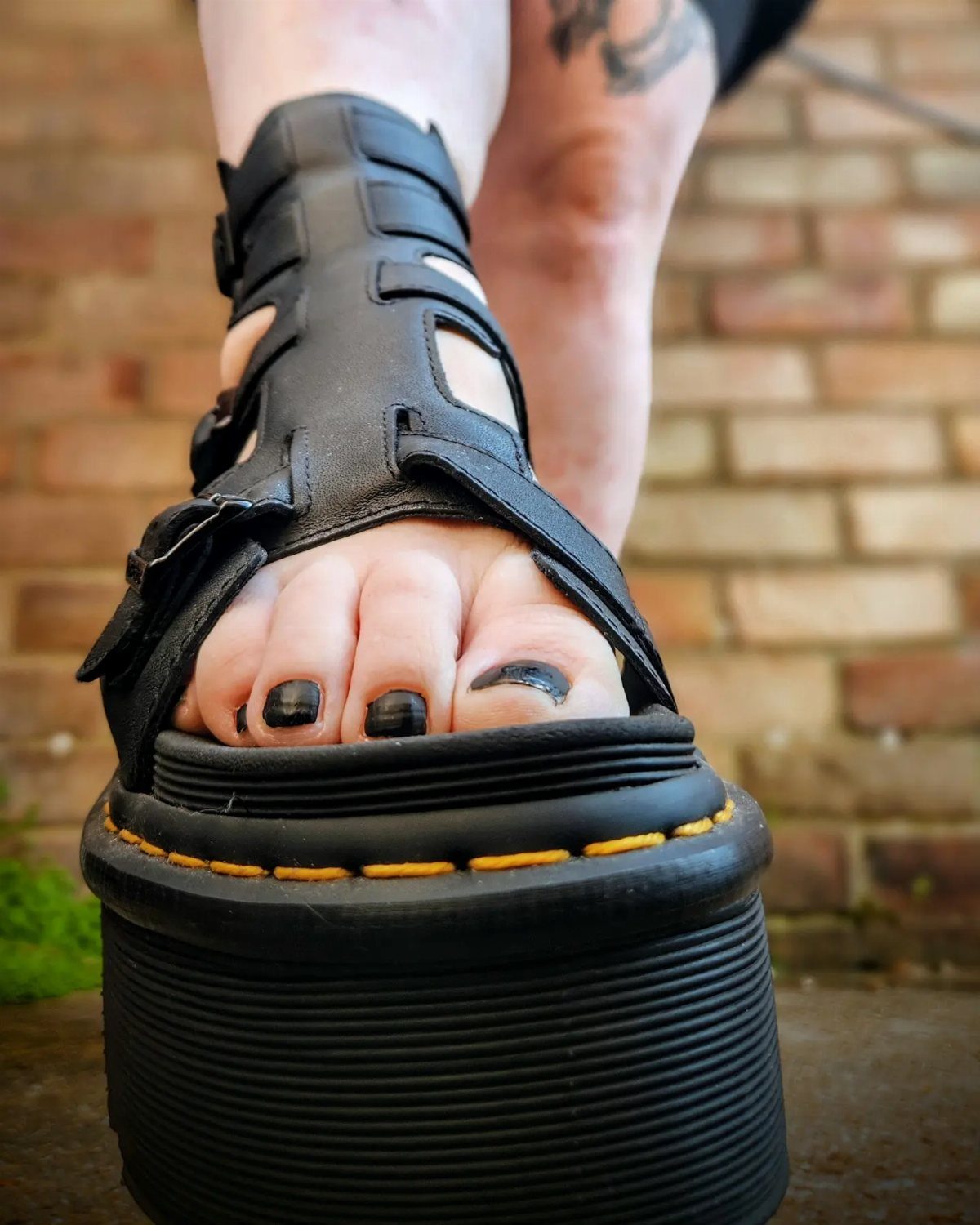 A person wearing chunky black leather platform sandals with wide straps and black nail polish.