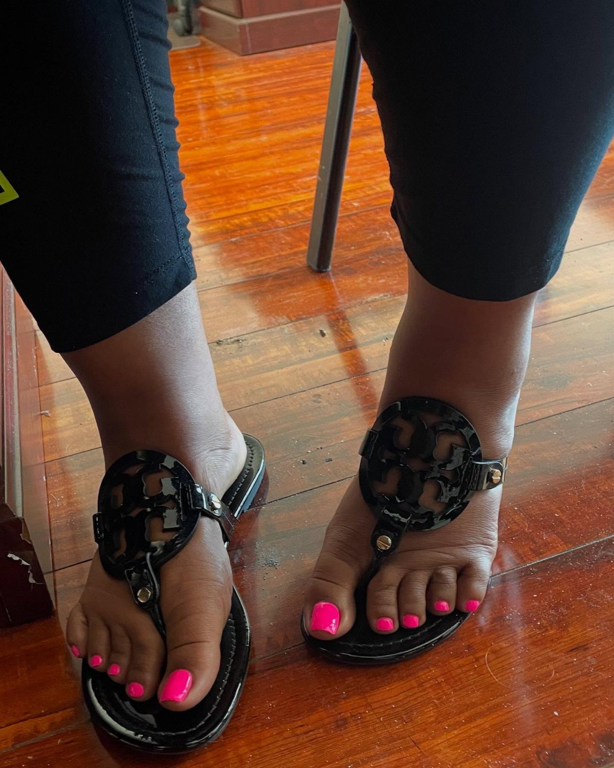 Black patent leather thong sandals worn by a person with bright pink nail polish.