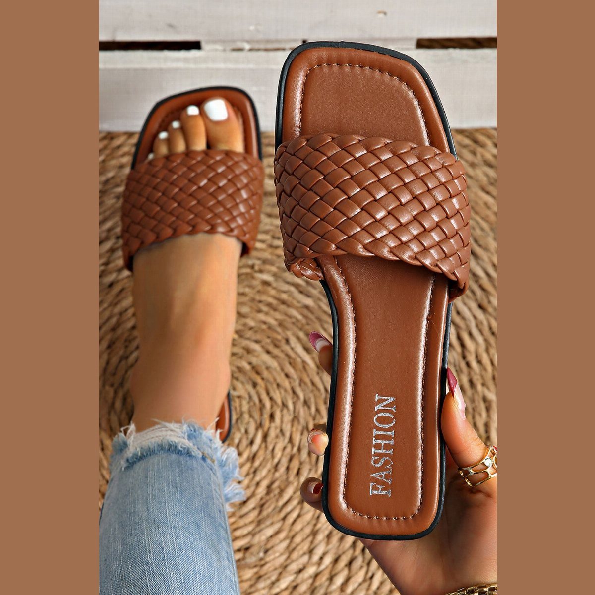 Tan braided leather slide sandals shown on a person's foot and held in a hand.