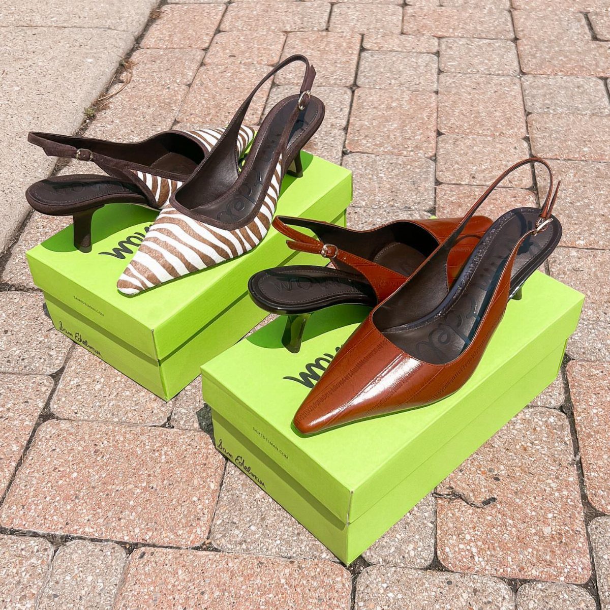 Two pairs of slingback heels resting on lime green shoeboxes on a brick walkway.