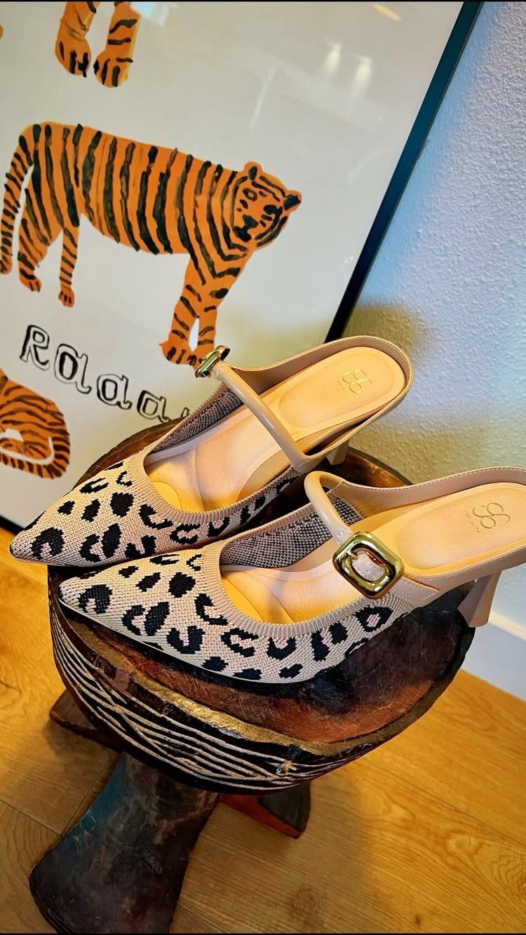 Leopard print slingback heels with gold buckles resting on a wooden pedestal.