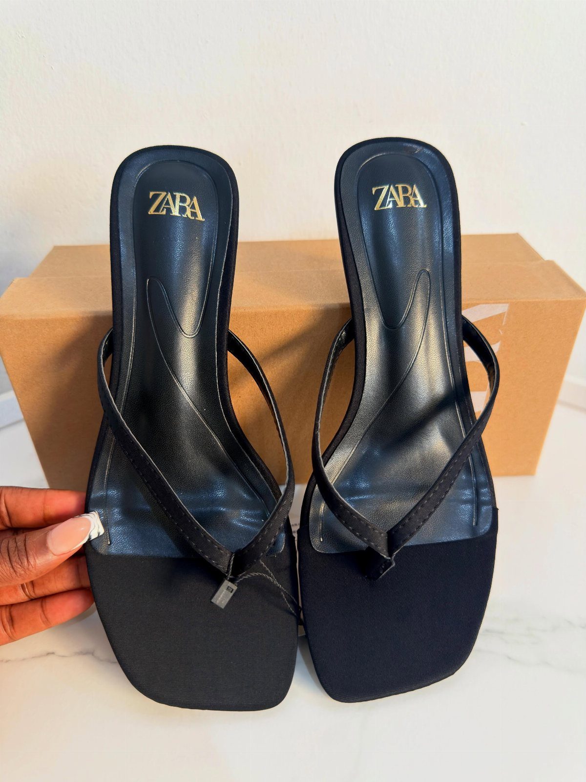 Black Zara thong-style high-heeled sandals resting on a white surface near a cardboard box.