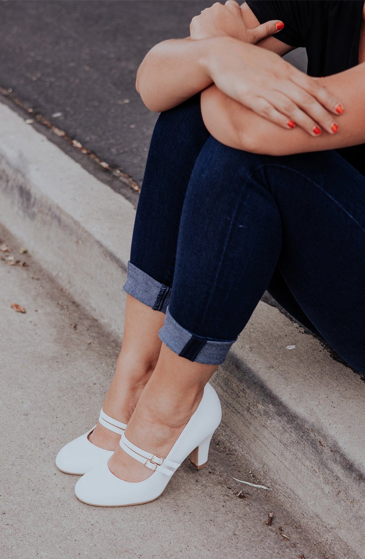 White Mary Jane heels with thin straps worn by a person in blue jeans.
