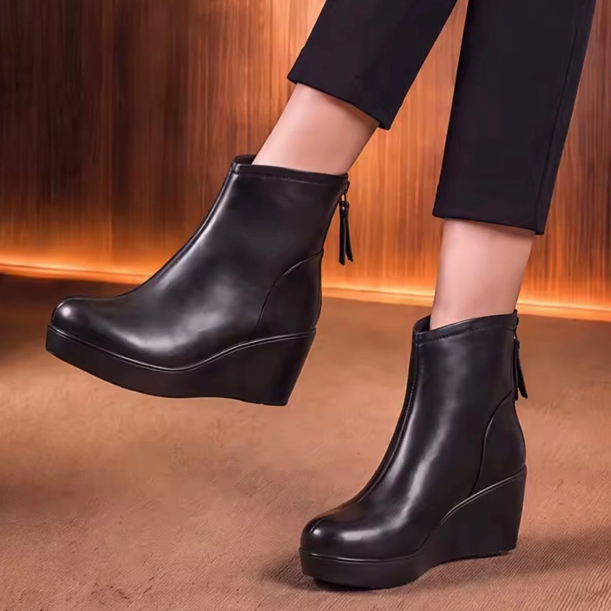 Black leather wedge ankle boots worn by a person standing against a wooden background.