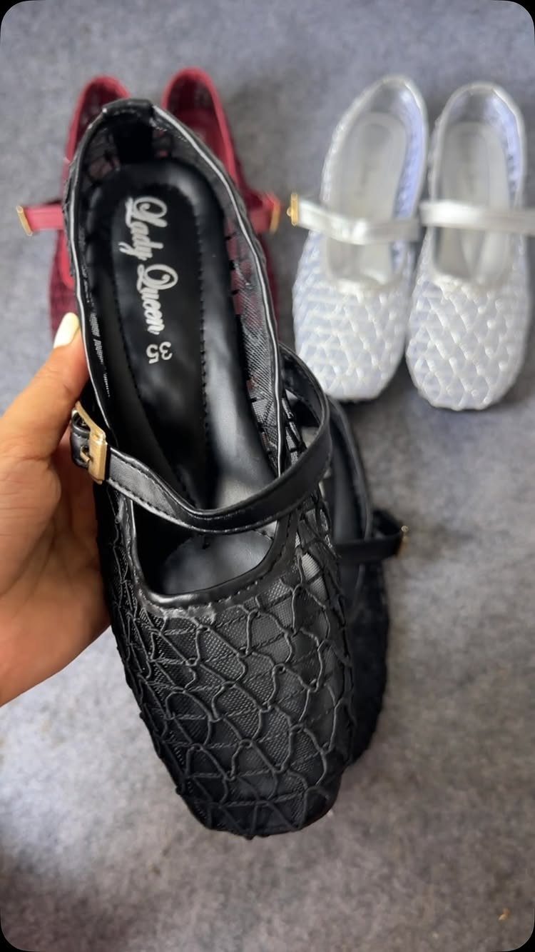Black mesh patterned flats held by a hand near white and red shoes.