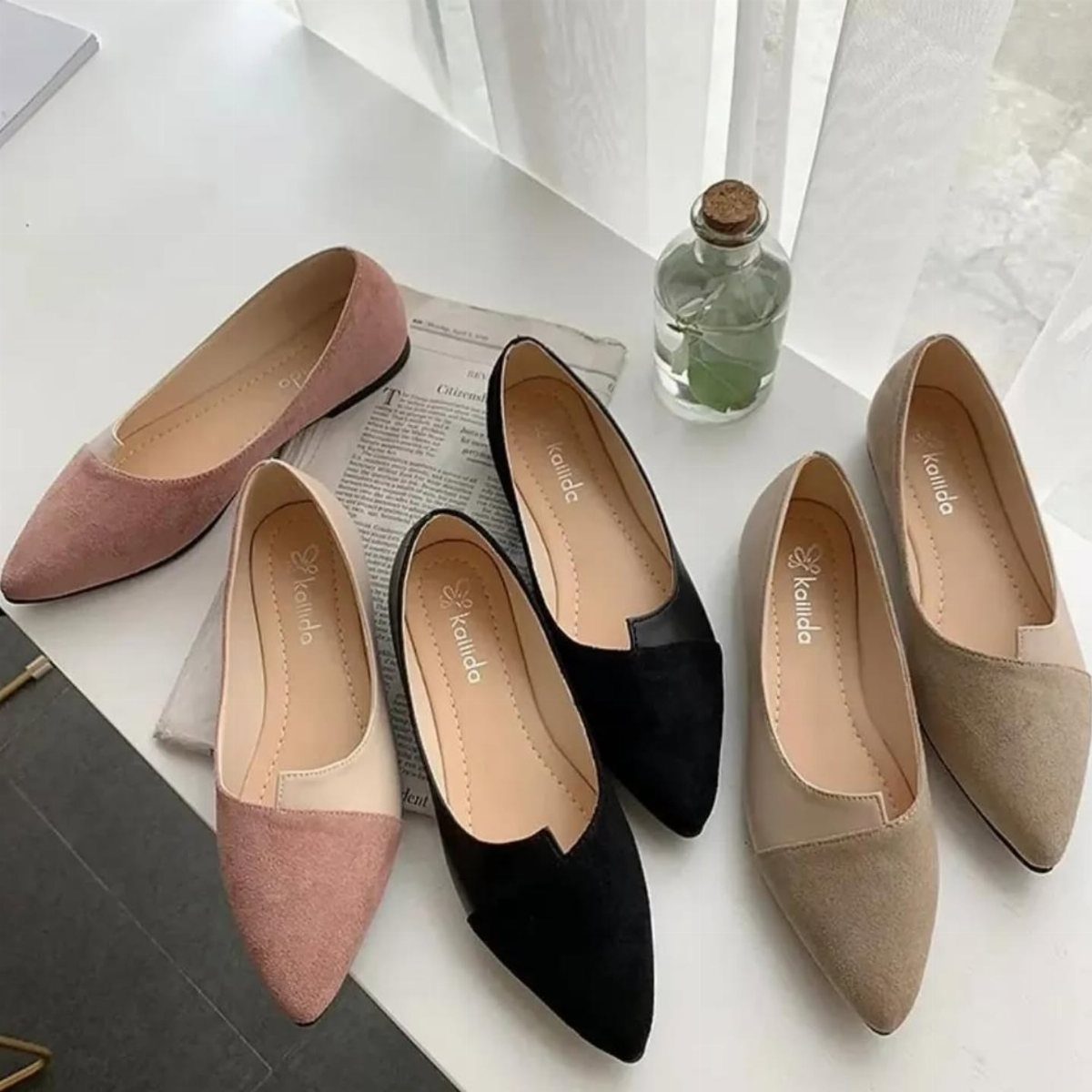 Six pairs of pointed-toe flats in pink, black, and beige arranged on a white table.