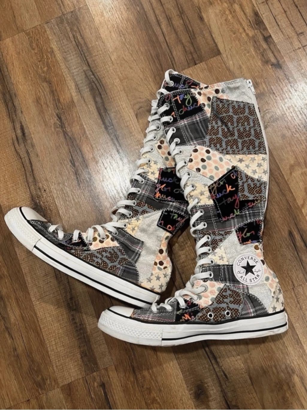Patchwork knee-high sneakers with various patterns resting on a wooden floor.