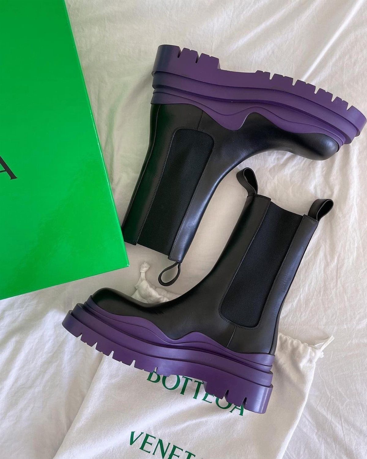 Black leather ankle boots with thick purple lug soles resting on white fabric.